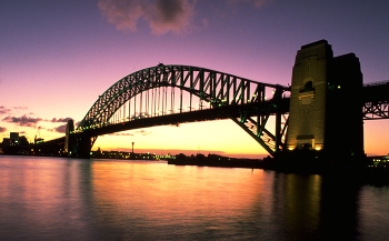 Sydney Harbour Bridge / The Harbour Bridge is as classic a symbol of Sydney as the shells of the Opera House itself.

Sydney Harbour Bridge, seen here at sunset, connects the Sydney central business district with the North Shore commercial and residential areas.

When completed, in 1932, the bridge Down Under was the widest bridge on the planet and the world's largest single-arch bridge; but was not the longest.

The single arch design was built from both ends (using cable supports) and joined in the middle.

Built to carry motor vehicles, trains, trams (until 1958), pedestrians and bicycles, the bridge's span of 1,650 feet allows unobstructed passage for ships in Sydney Harbour.

https://travelnotes.org/pics/Australia/05-Sydney_Harbour_Bridge.htm