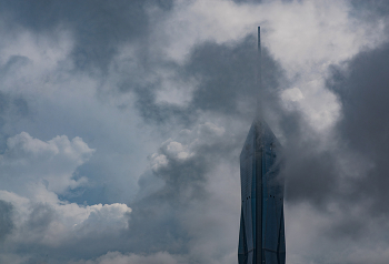 Merdeka 118 Tower Rising Through the Clouds, Kuala Lumpur / The Merdeka 118 Tower in Kuala Lumpur, Malaysia, rises through dramatic clouds, with its sleek glass facade and spire piercing the sky. The moody atmosphere and partially obscured view highlight the tower’s height and architectural elegance against a backdrop of swirling clouds.